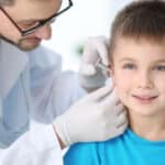 Medico pediatra controlla l'orecchio di un bambino durante una visita domiciliare